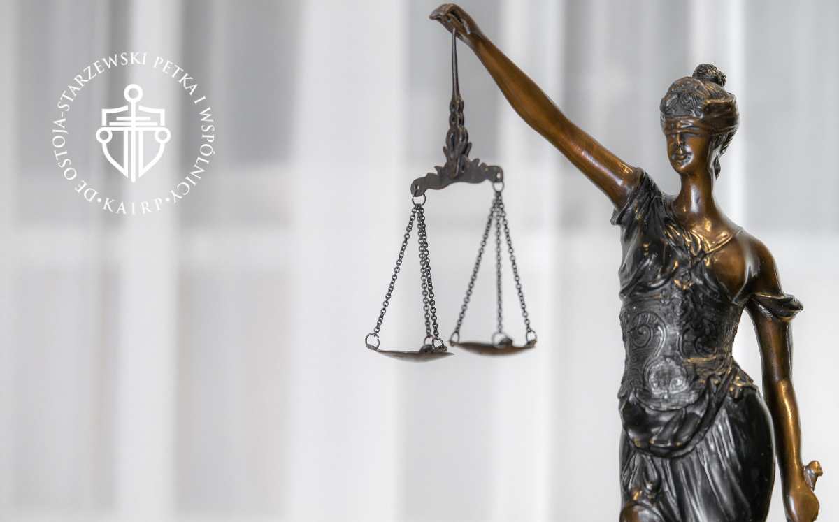 Statua Temidy z wagą symbolizującą sprawiedliwość, na tle rozmytego wnętrza sądu.