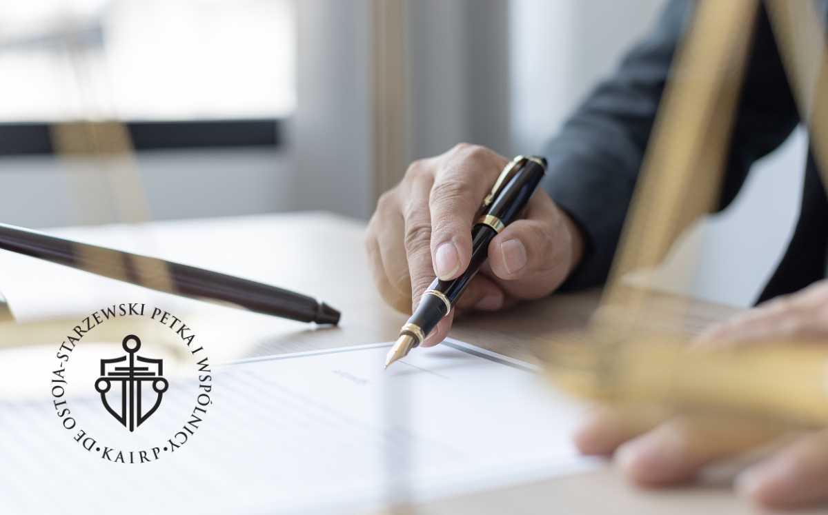 Mężczyzna podpisuje dokument prawniczy w kancelarii, na pierwszym planie waga Temidy.