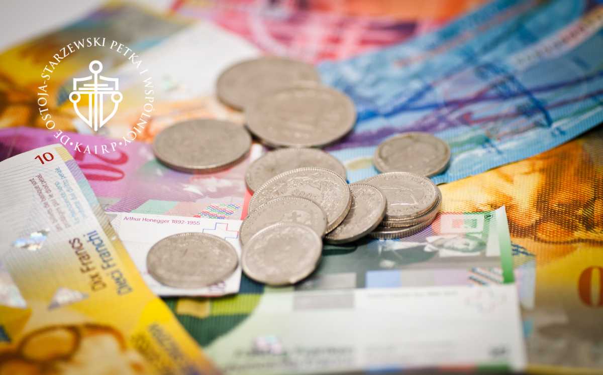 Szwajcarskie franki i monety rozrzucone na stole. Na zdjęciu widoczne logo kancelarii Ostoja-Starzewski Petka i Wspólnicy.