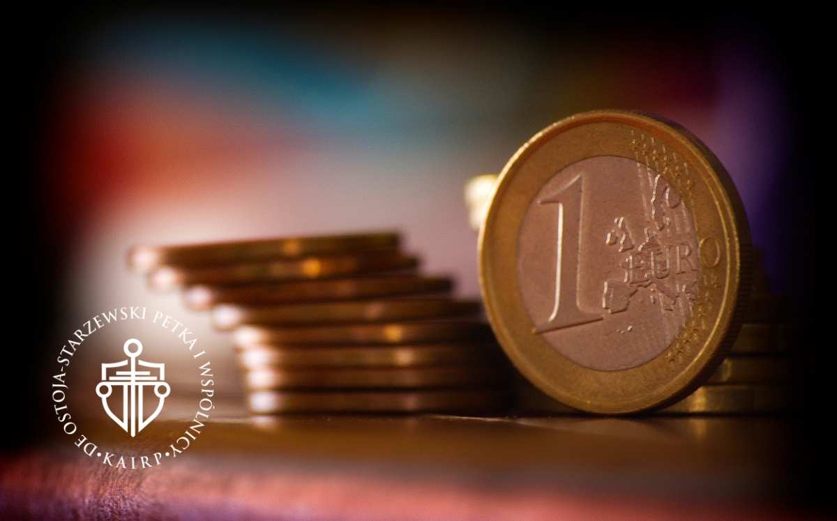 Stos monet euro, na pierwszym planie moneta o nominale 1 euro, w tle rozmyte kolory.