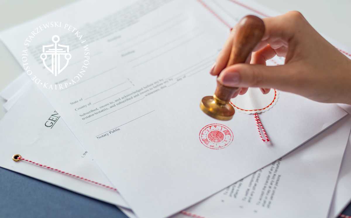 sankcja-kredytu-darmowego-co-z-twoja-umowa Ręka przykłada pieczątkę notarialną na dokumencie, obok widoczne zszyte umowy prawnicze.