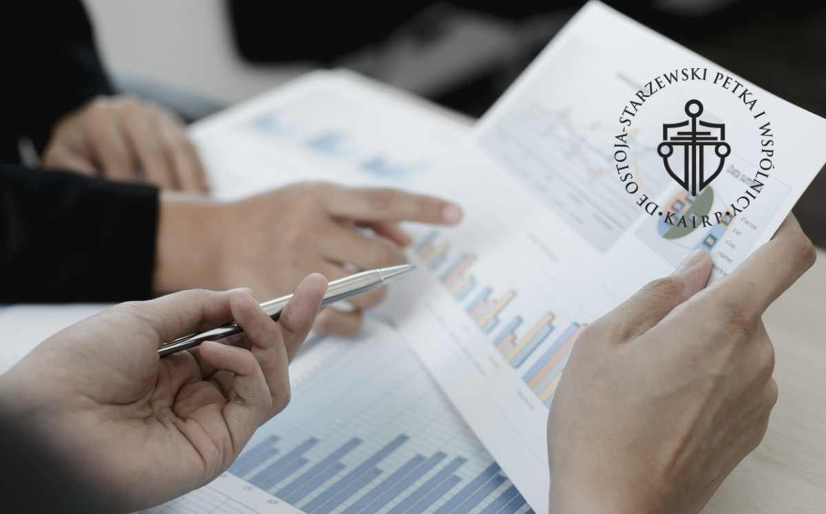 analiza-umowy-kredytu-konsumenckego Dwie osoby analizują wykresy i dokumenty finansowe przy biurku, omawiając warunki umowy kredytowej; na zdjęciu widoczne logo kancelarii De Ostoja-Starzewski Petka i Wspólnicy.
