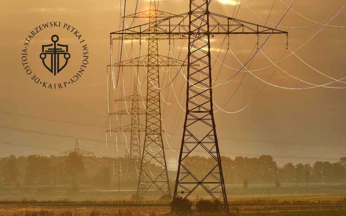 Linie wysokiego napięcia i stalowe słupy przesyłowe stojące na otwartym polu podczas zachodu słońca.