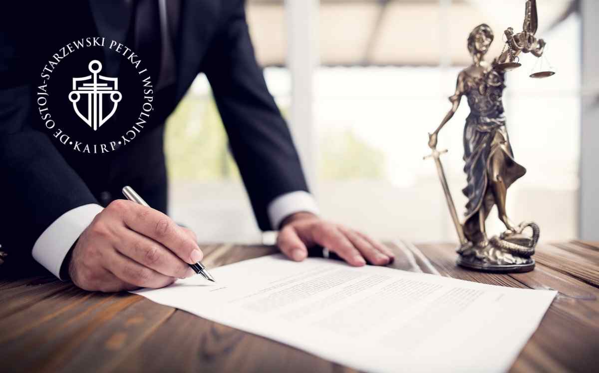Prawnik podpisujący dokument ugody przy biurku, obok statuetka Temidy symbolizująca sprawiedliwość