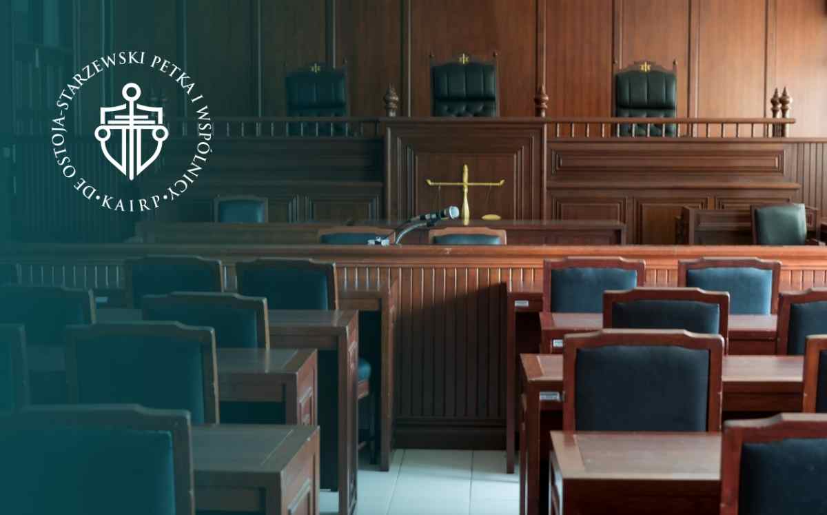 Sala rozpraw sądowych z ławą sędziowską, wagą sprawiedliwości i miejscami dla uczestników postępowania.