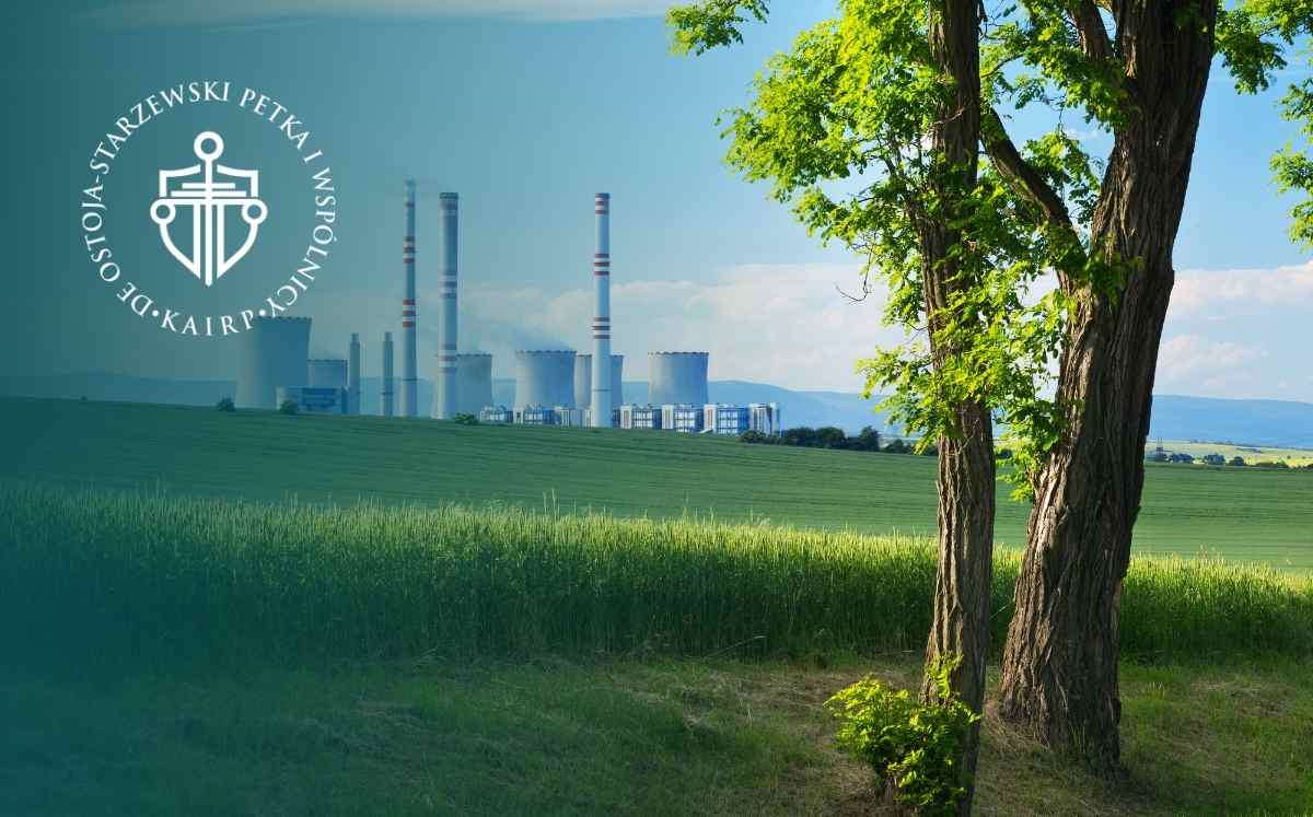 Elektrownia widoczna w oddali na tle pól i drzew – krajobraz z instalacją energetyczną i infrastrukturą przesyłową.