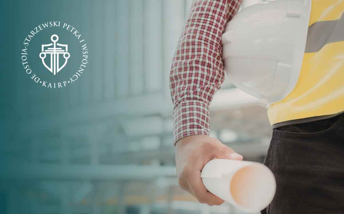 Pracownik budowlany w kamizelce odblaskowej i kasku trzyma zwinięty projekt budowlany.