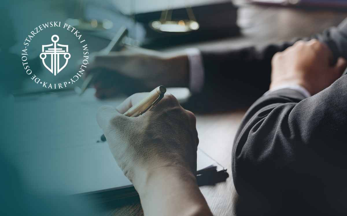 Prawnik sporządzający dokumenty przy biurku w kancelarii, w tle widoczne logo firmy