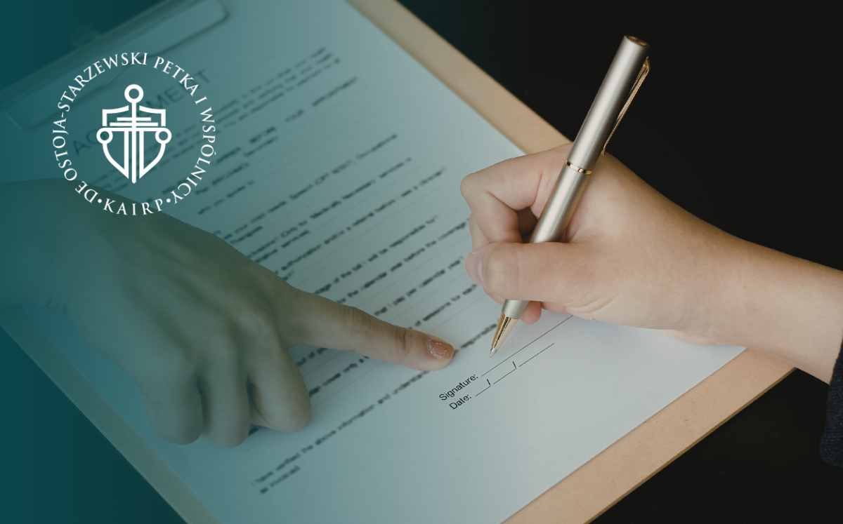 Osoba podpisująca dokument długopisem, druga ręka wskazuje miejsce podpisu – scena zawierania umowy.