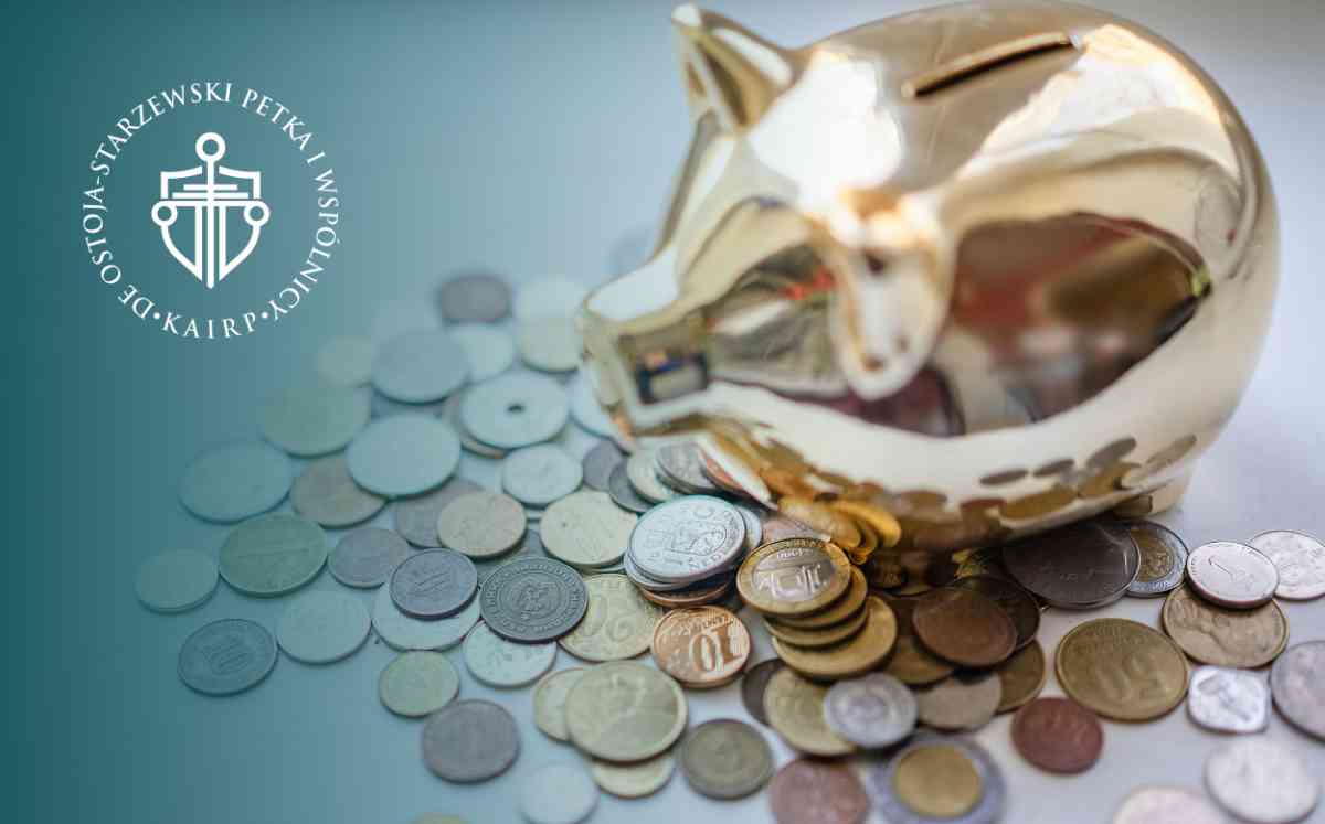 Złota skarbonka w kształcie świnki stojąca na rozsypanych monetach o różnych nominałach.