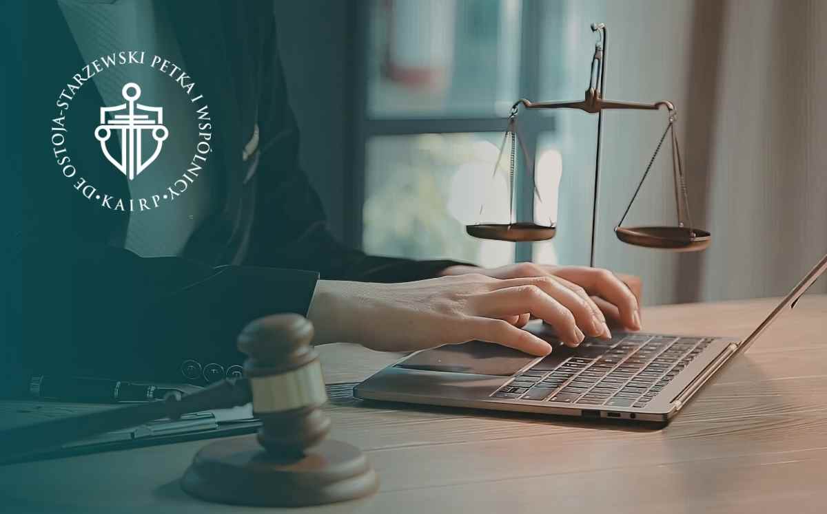 Dłonie osoby pracującej na laptopie obok wagi sprawiedliwości i młotka sędziowskiego, z logo kancelarii po lewej stronie.