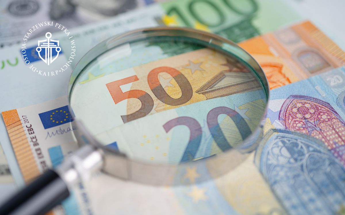 Szkło powiększające nad banknotami euro, podkreślające banknot 50 euro, symbolizujący analizę finansową.