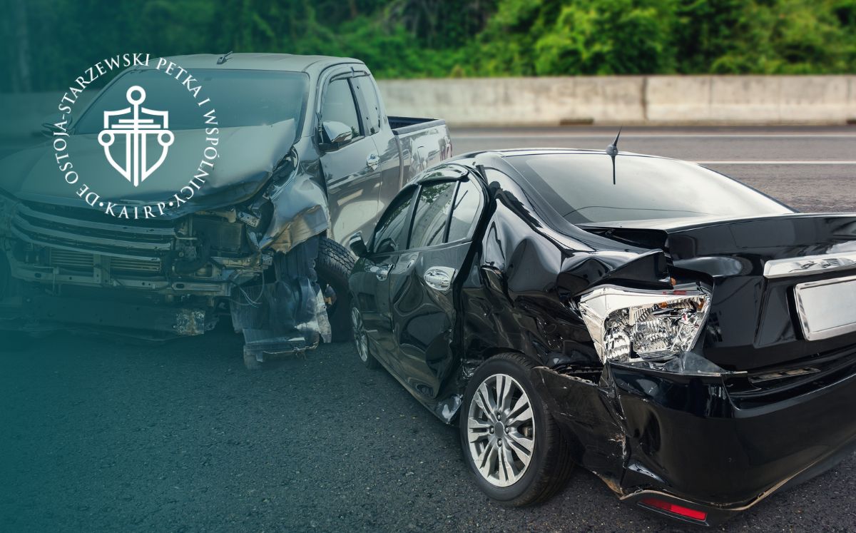 Dwa samochody brały udział w wypadku na autostradzie: czarny sedan z poważnymi uszkodzeniami z tyłu i jasny pick-up z uszkodzonym przodem, na utwardzonej drodze z zieloną barierą.