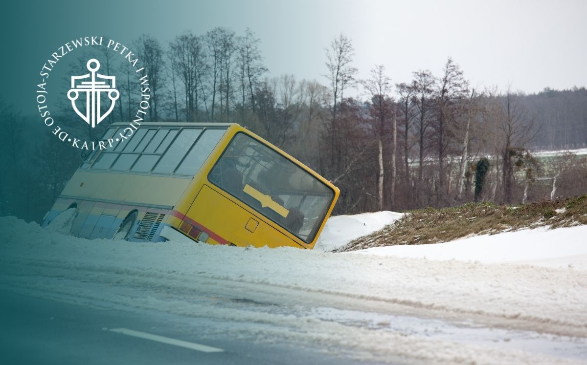 Żółty autobus leży na poboczu zaśnieżonej drogi. W tle widać drzewa i wzgórze